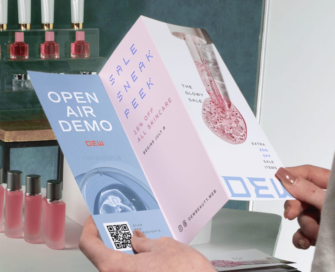 Person holding cosmetic company brochure promoting discount prices with cosmetics in the background