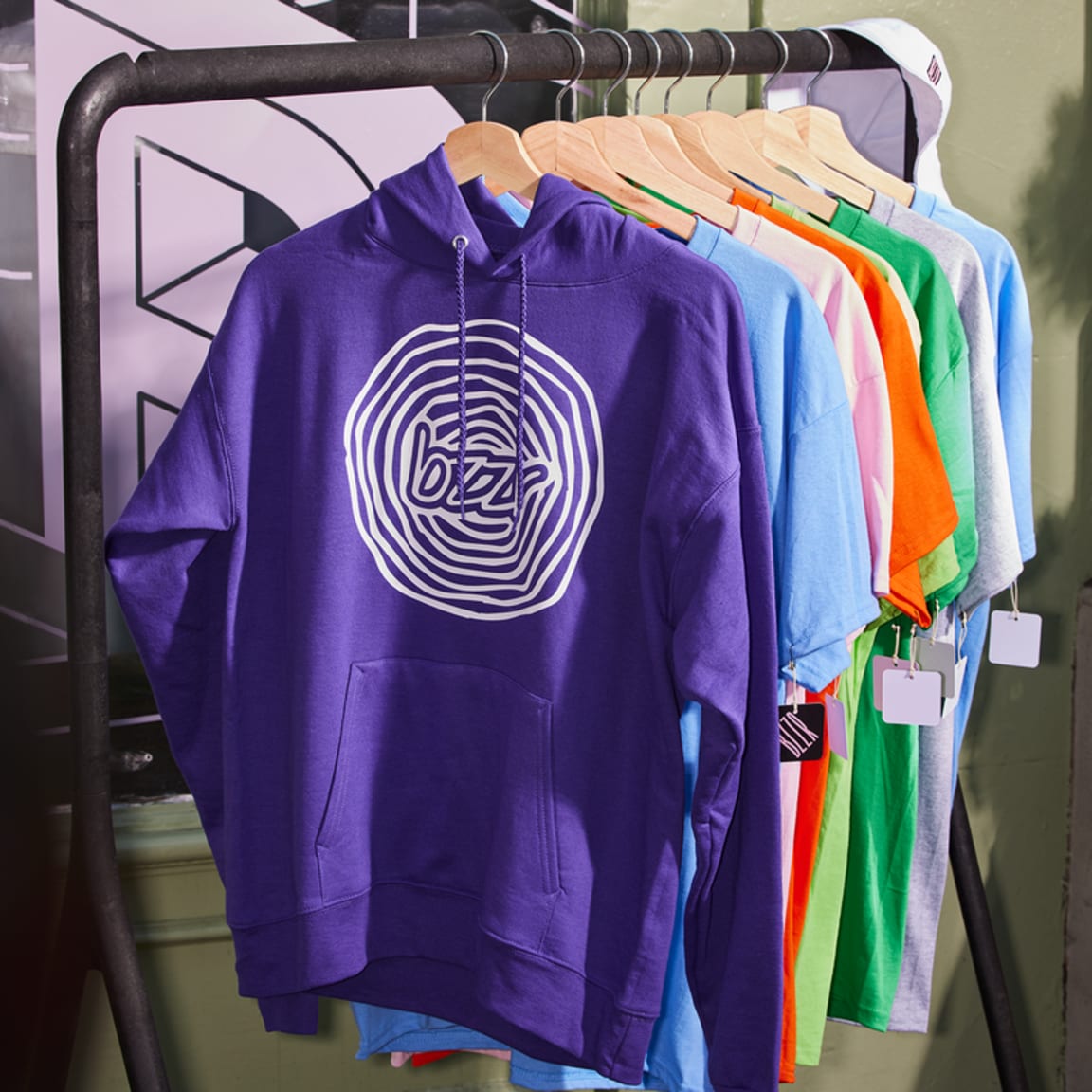 A rail with hanging T-shirts and a purple hoodie with a white swirling circle design
