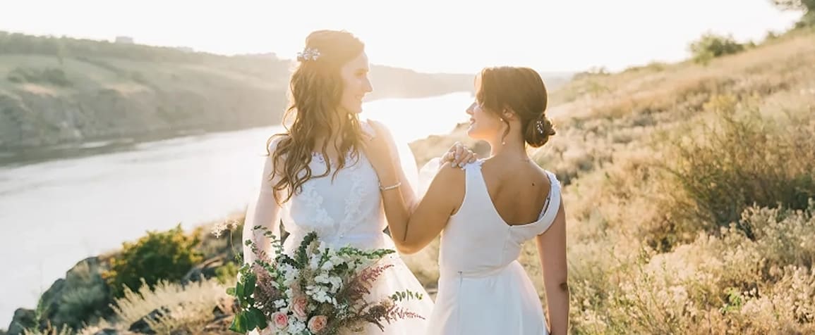 Wedding couple in white looking at each other and smiling with beautiful sunny landscape in background