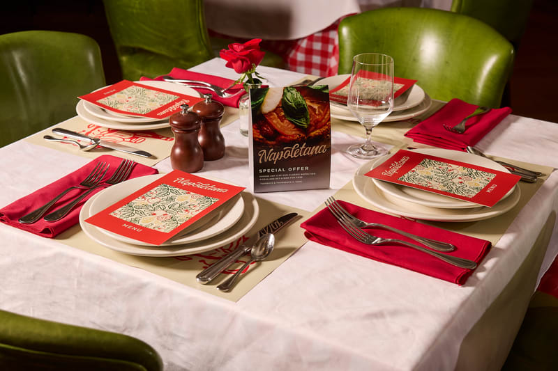 Holiday restaurant table setting with red napkins, custom printed menus and a promotional table card.