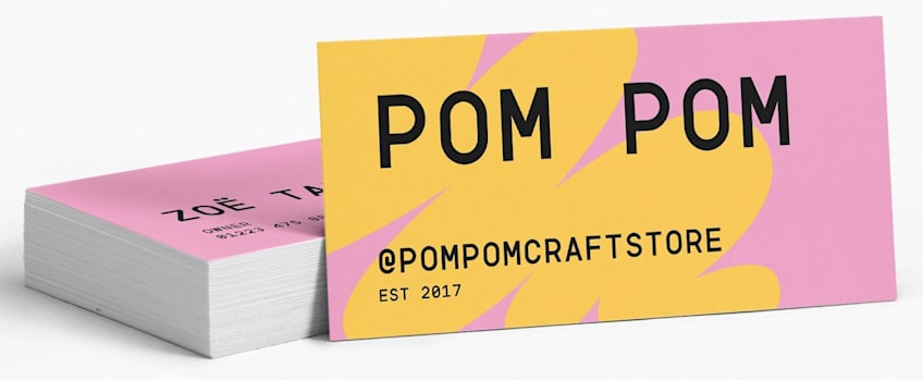 Stack of colorful pink and yellow branded mini business cards featuring bold typography for Pom Pom Craft Store.