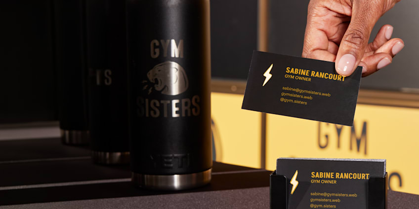 Hand holding charcoal black business card with yellow lightning bolt logo and yellow contact details for gym small business owner