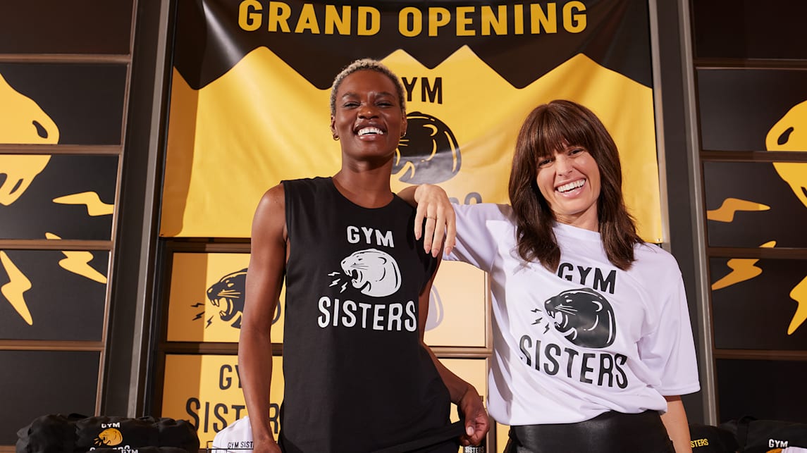 Gym business owners wearing branded merch with logos in front of branded signage