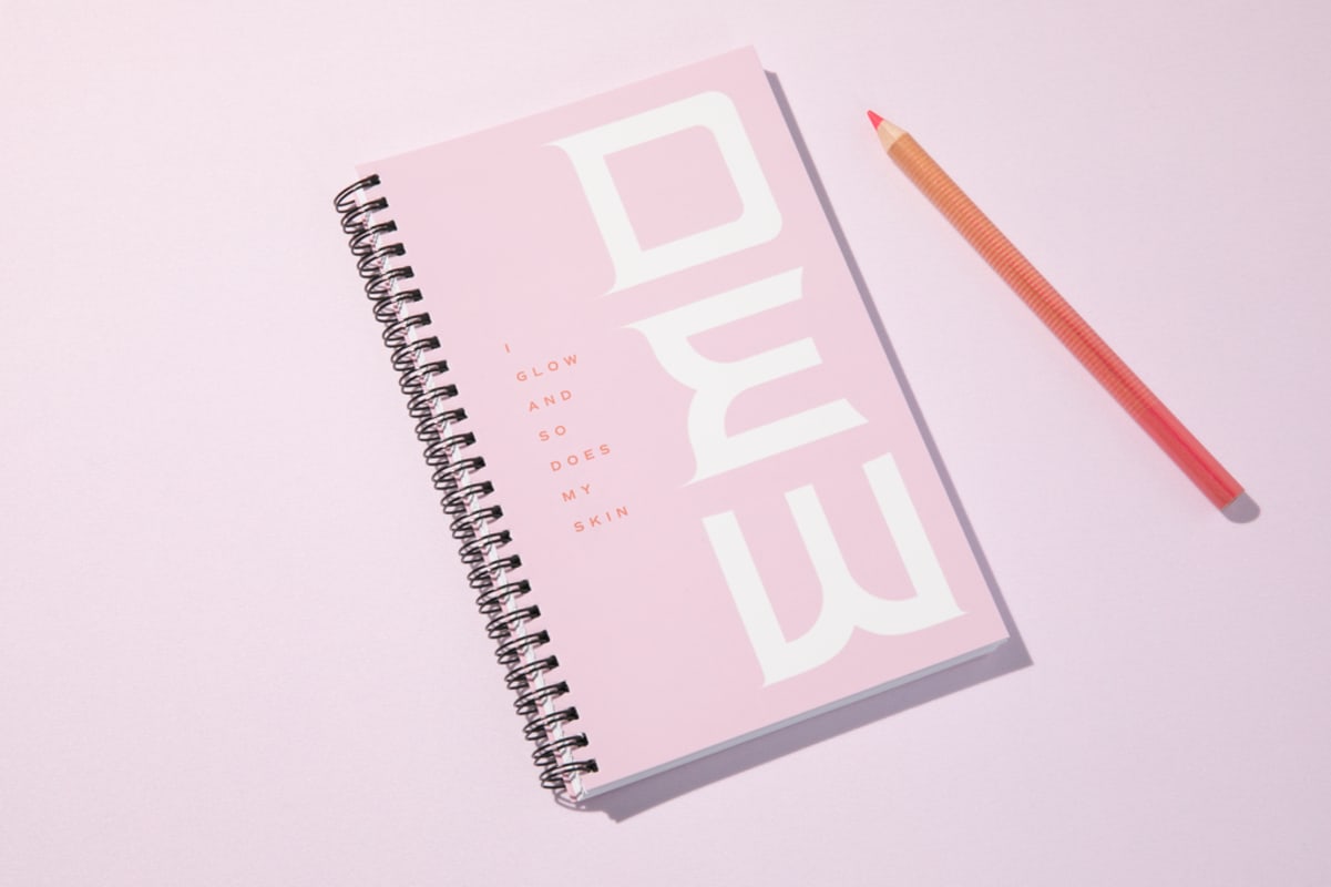 Light pink branded notepad and pencil with pink background.