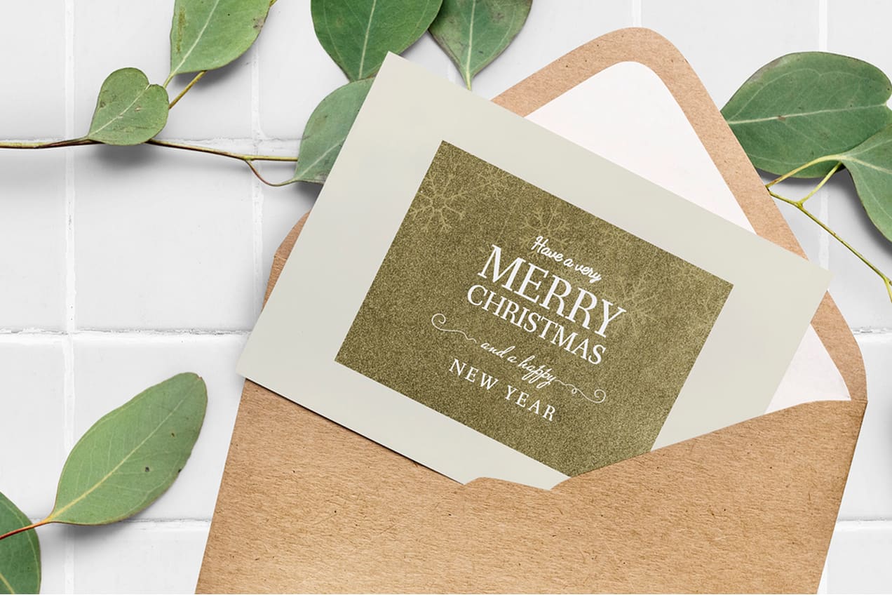 Green card with rustic feel sticking out of a kraft paper envelope surrounded by greenery.
