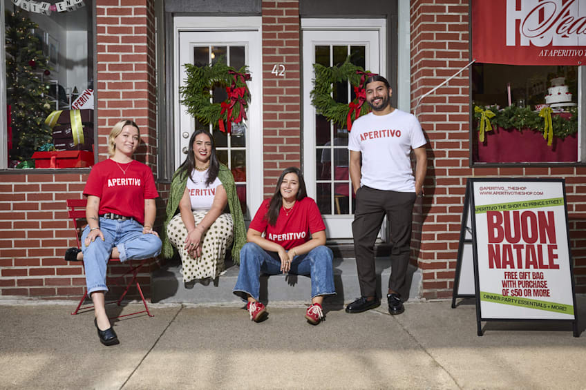 Business employee standing in front of the decorated storefront, next to an A-Frame sign promoting a business holiday event