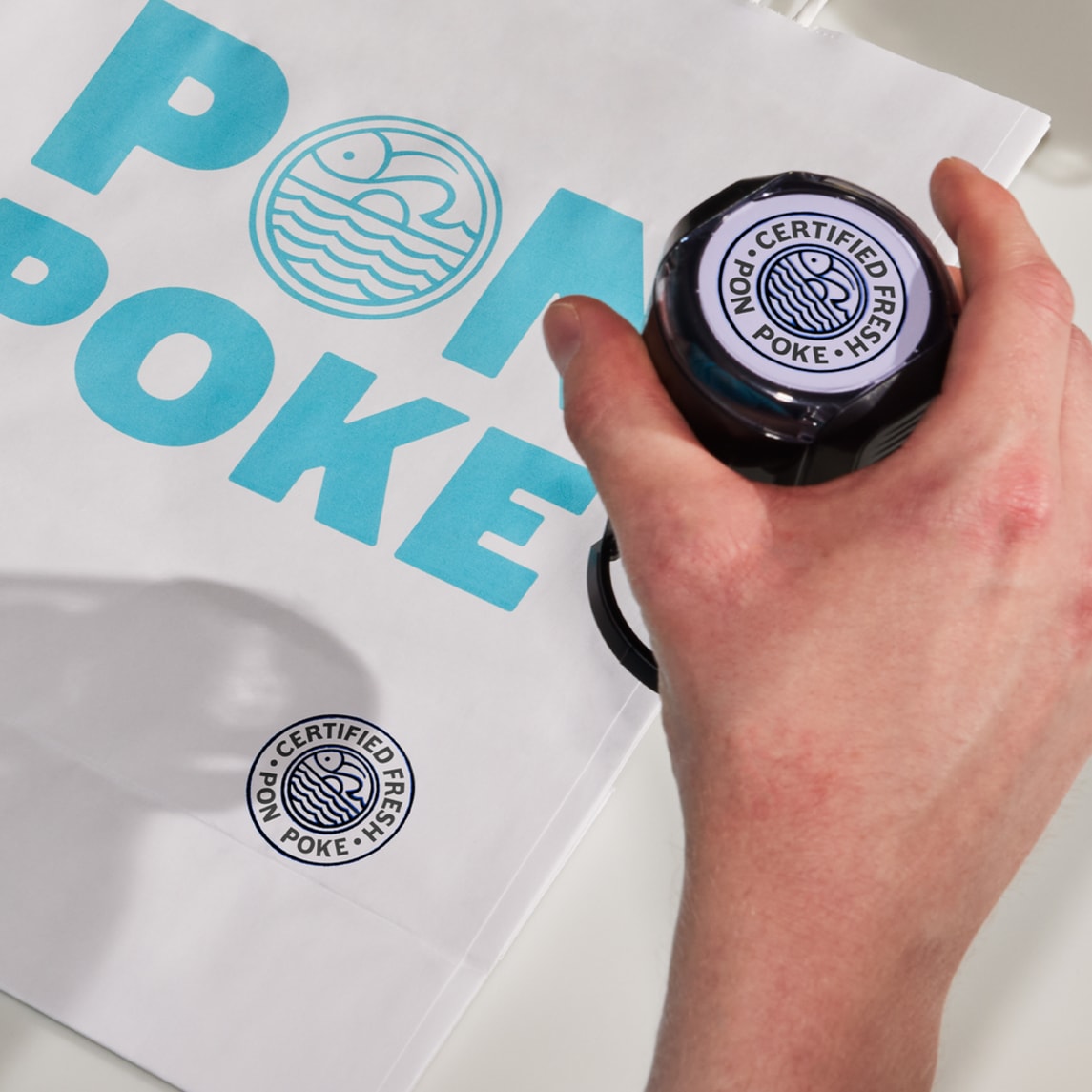 A blue poke restaurant logo on a paper bag and a stamp