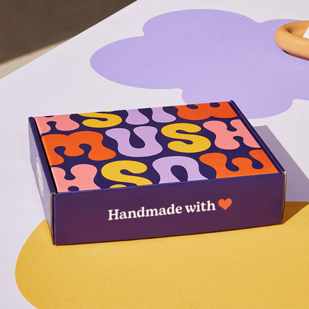 Closed purple custom mailer box with colorful design on exterior top panel and simple white text on front and side panels