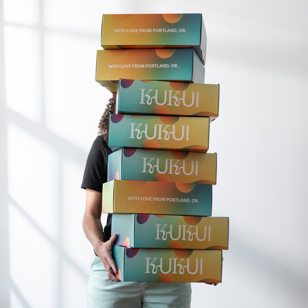 A person holding a tall stack of multicolored branded cardboard boxes.