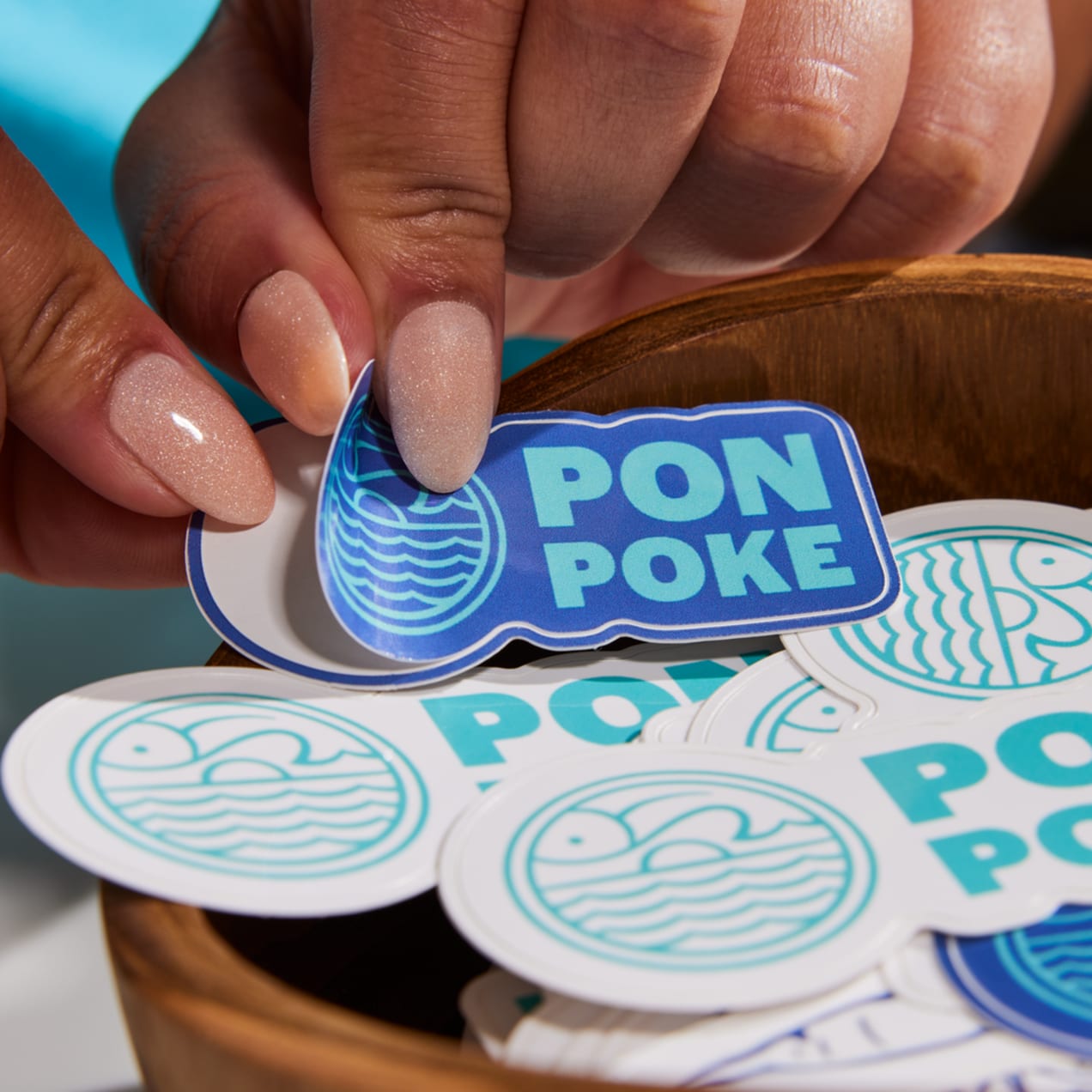Close up of hands peeling a blue branded poke shop sticker from a stack