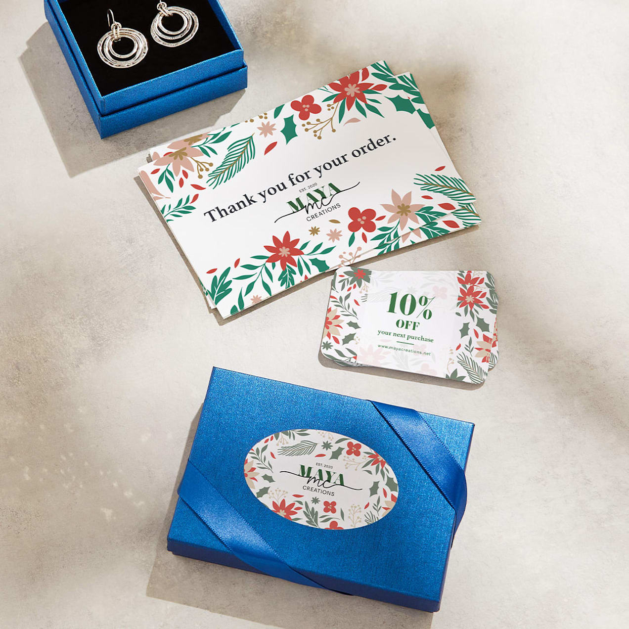 Silver earrings in a blue box, with a branded sticker on the lid and matching branded thank-you and discount cards