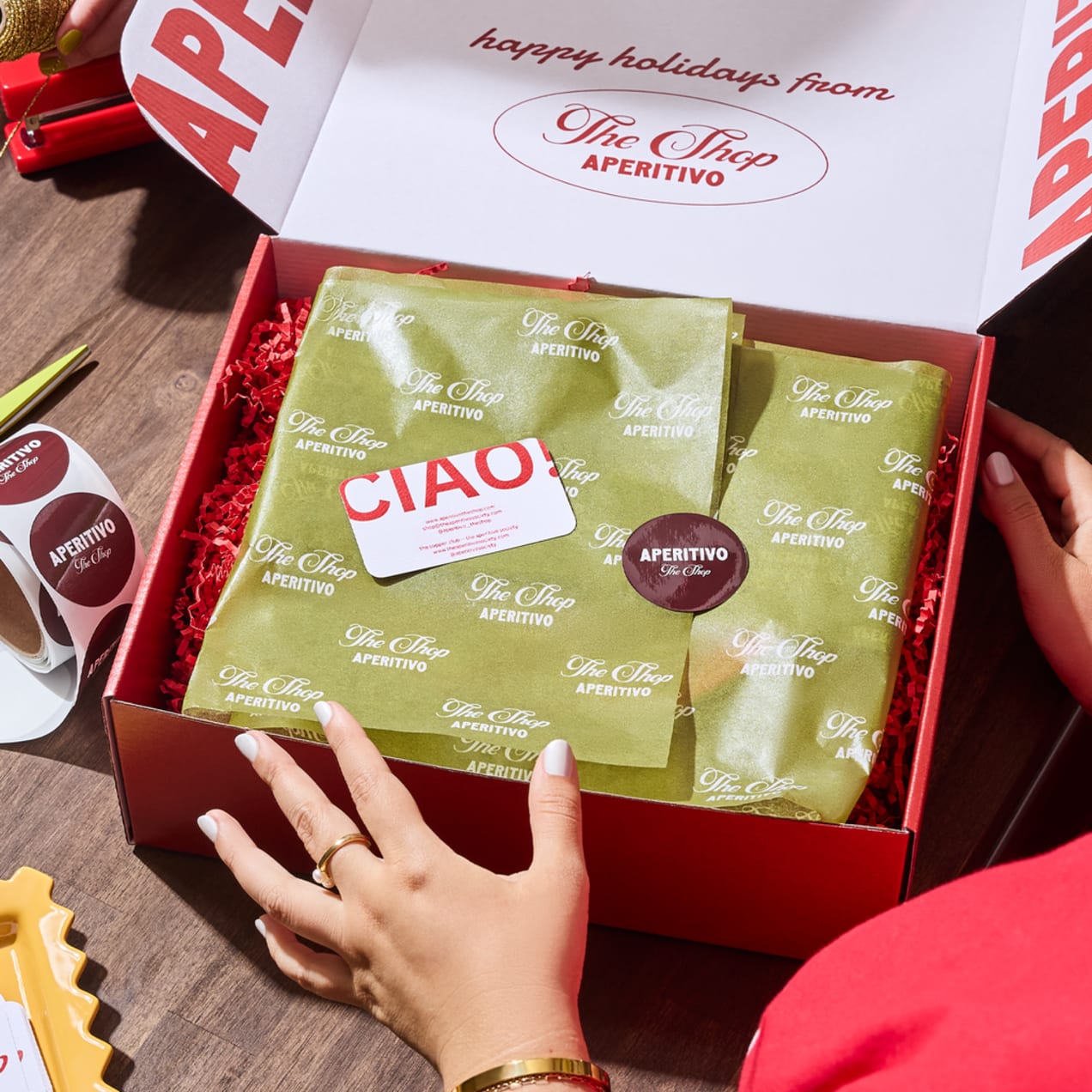A red box packaged with green paper and festive colored stickers and cards