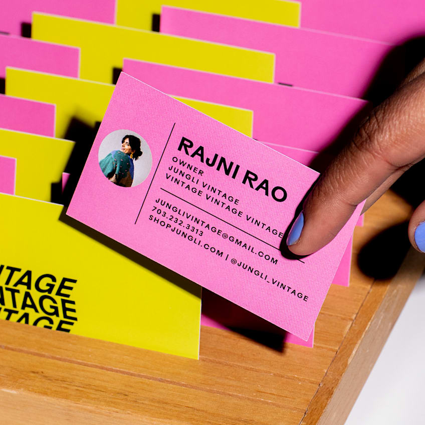A row of hot-pink and bright-yellow colored business cards printed on textured paper, a person holding a pink one in their hands
