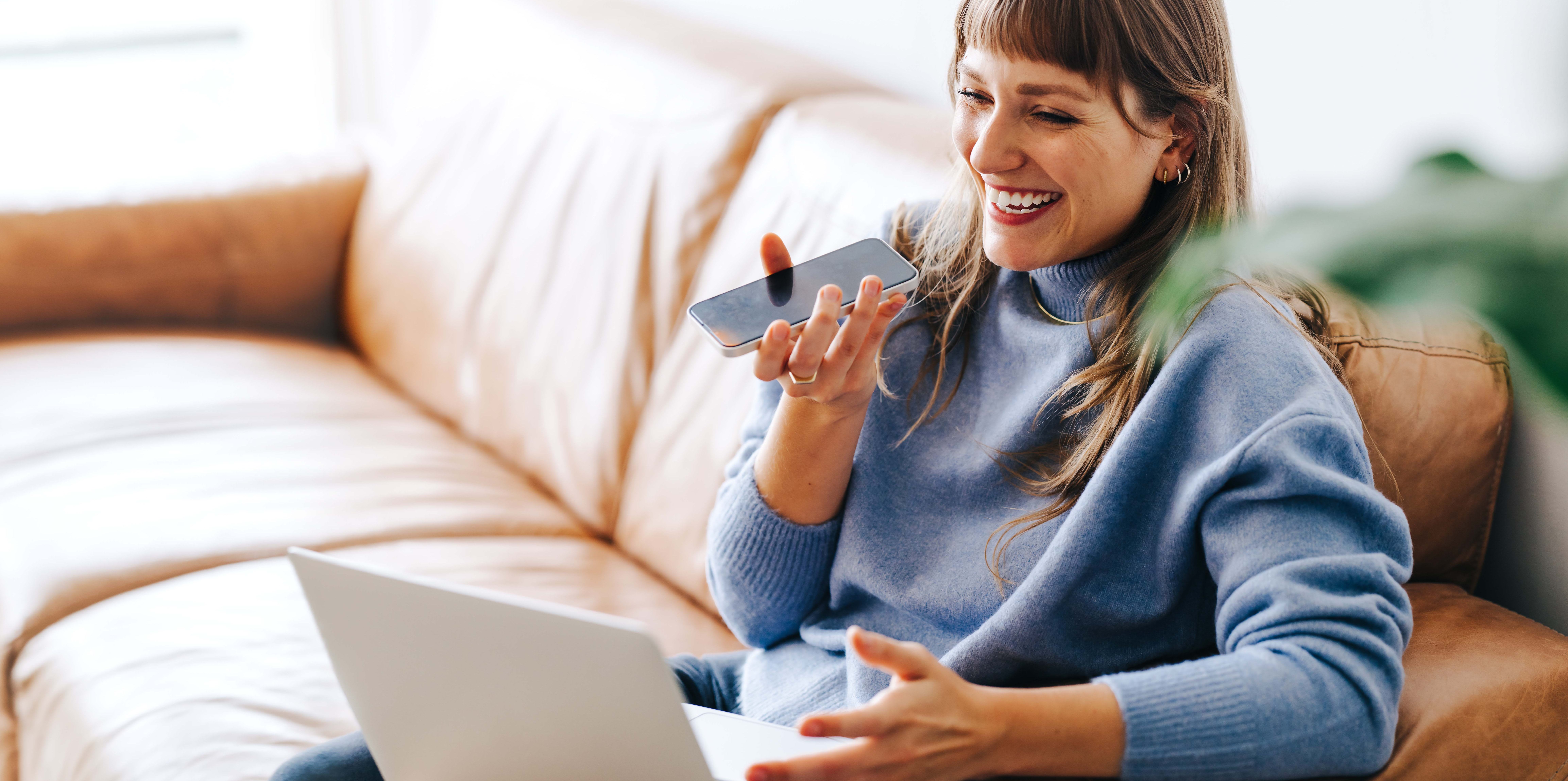 Frau mit Handy und Laptop auf Sofa