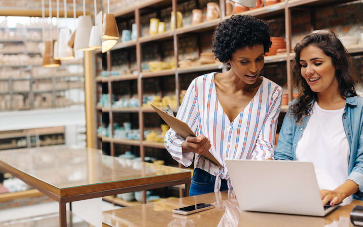 Two women business owners talk and look at a laptop