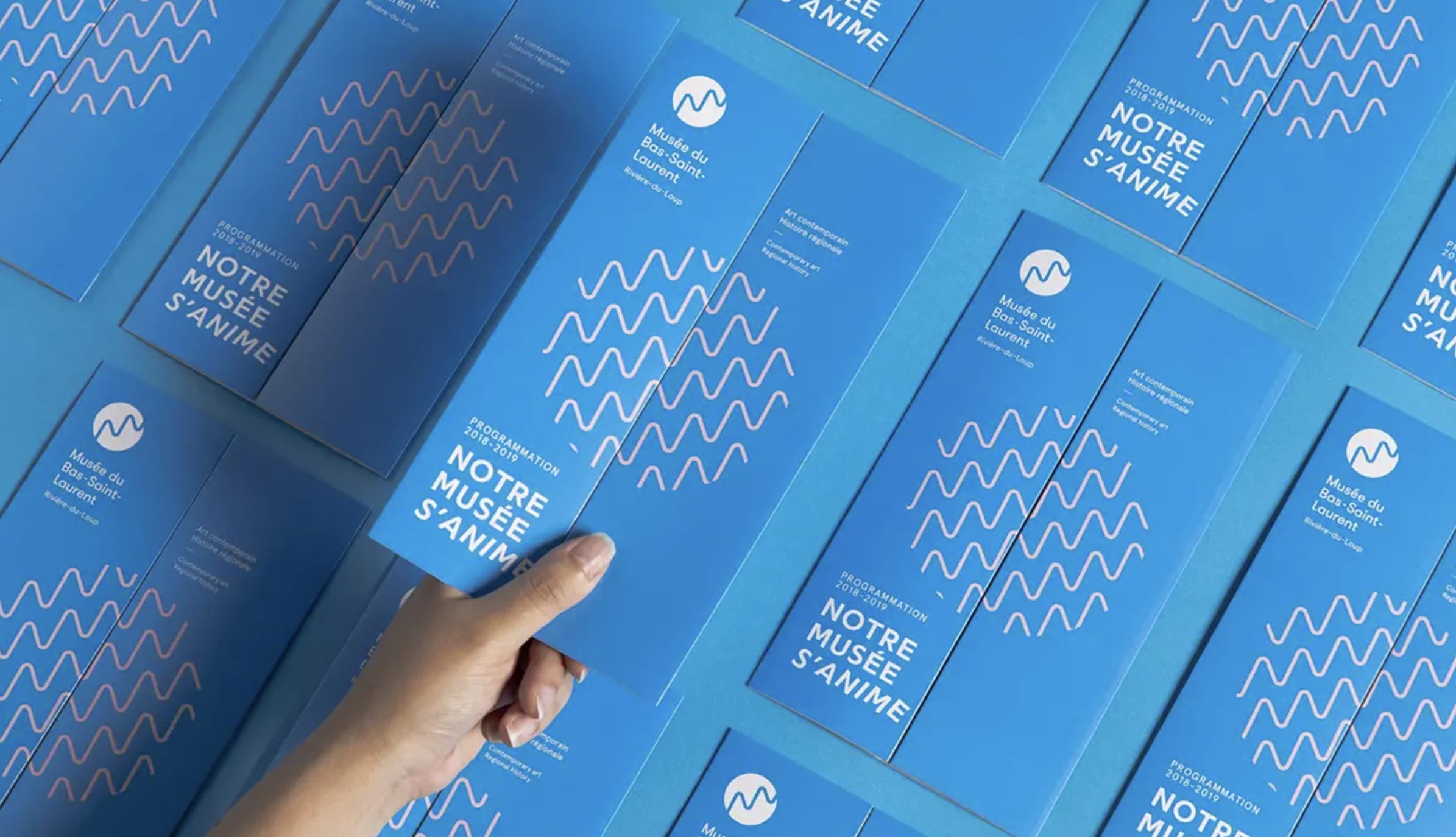 A hand picking up one of a number of Musée du Bas-Saint-Laurent brochures