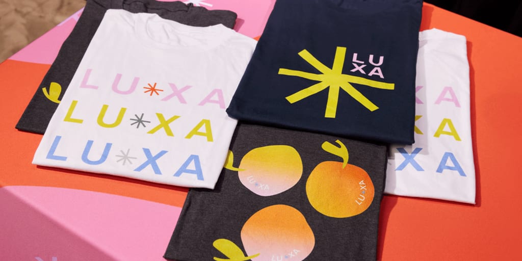 Promotional T-shirts in various colors with bold logos and text on a pink gradient background.