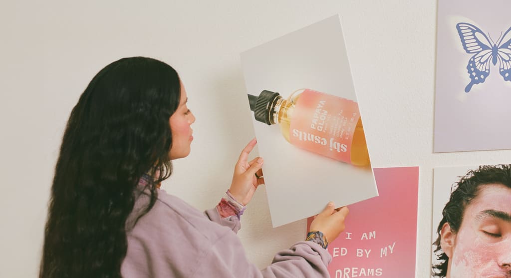Woman hanging a small framed product image alongside coordinated frames, symbolizing brand positioning.