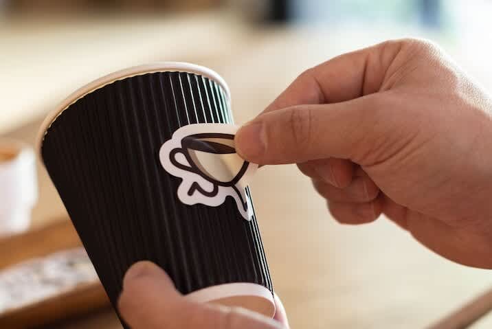 A small business owner putting a die-cut custom sticker on a coffee cup