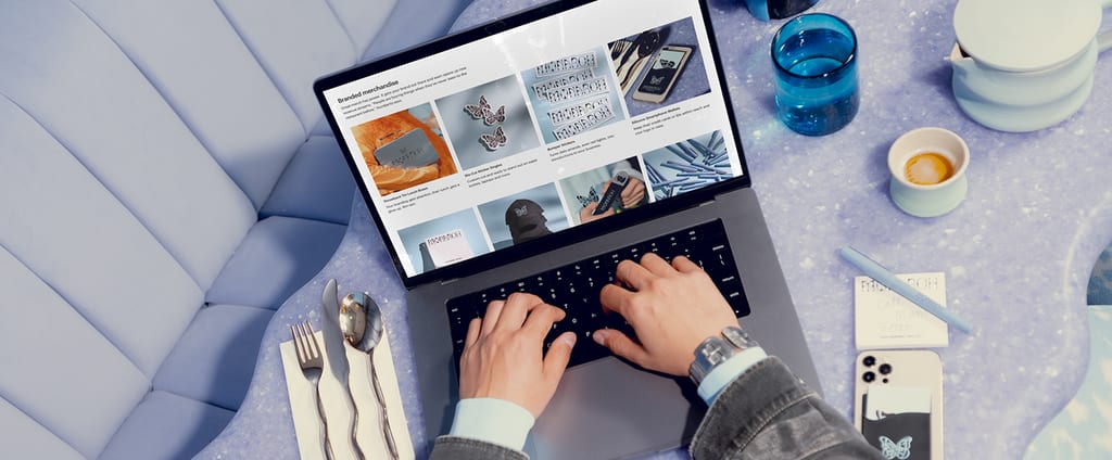 Remote work in a café: hands typing on a laptop with utensils, a glass, and a coffee cup on the table – e-commerce in action.