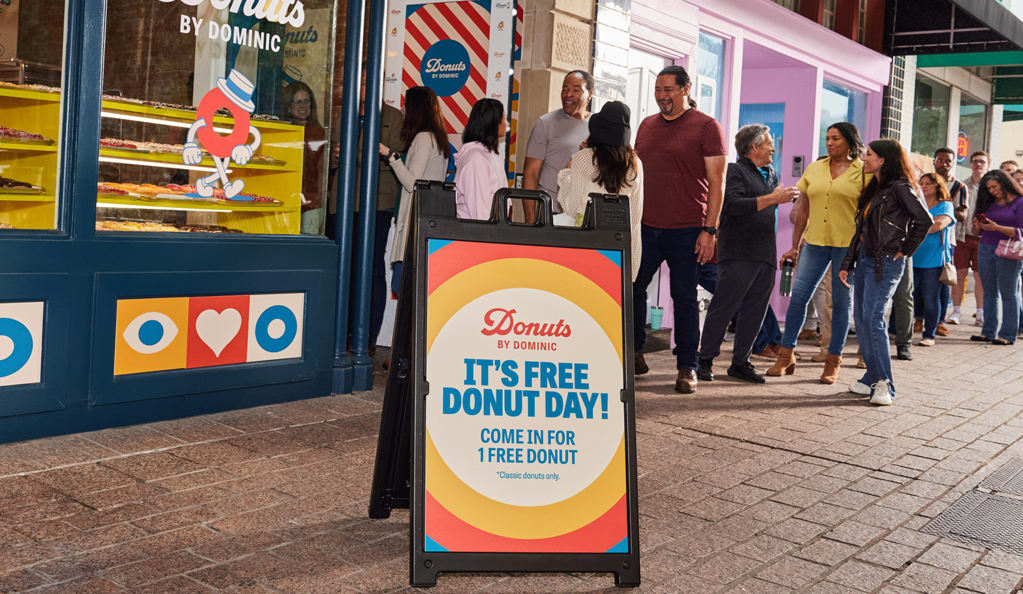 Colorful donut shop entrance featuring a branded outdoor advertising A sign with logo and matching brand colors.