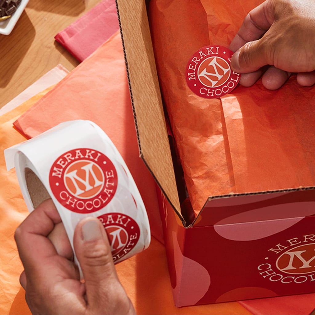 Hands pressing branded stickers down on their gifts wrapped in holiday packaging