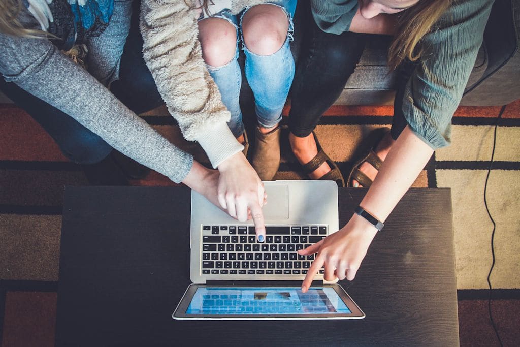 Three women sitting at a laptop, pointing at the screen.