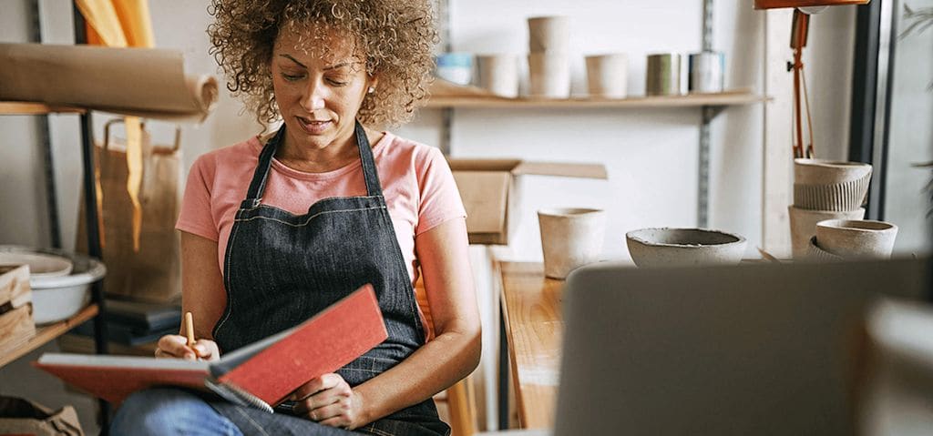 Woman taking notes in a red notebook at her pottery store.