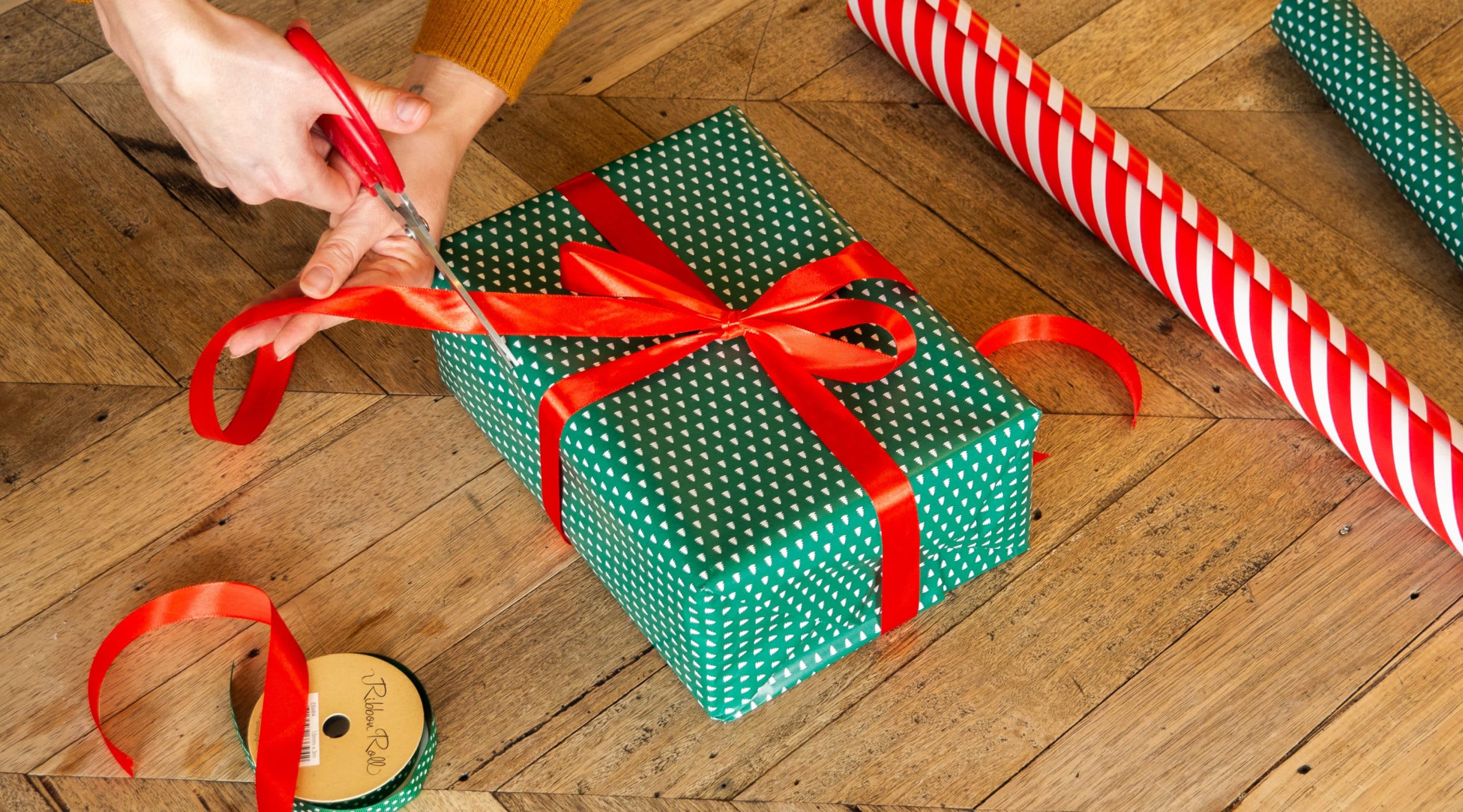 EIne Person trimmt die Enden eines Geschenkbandes nach dem Binden der dekorativen Schleife