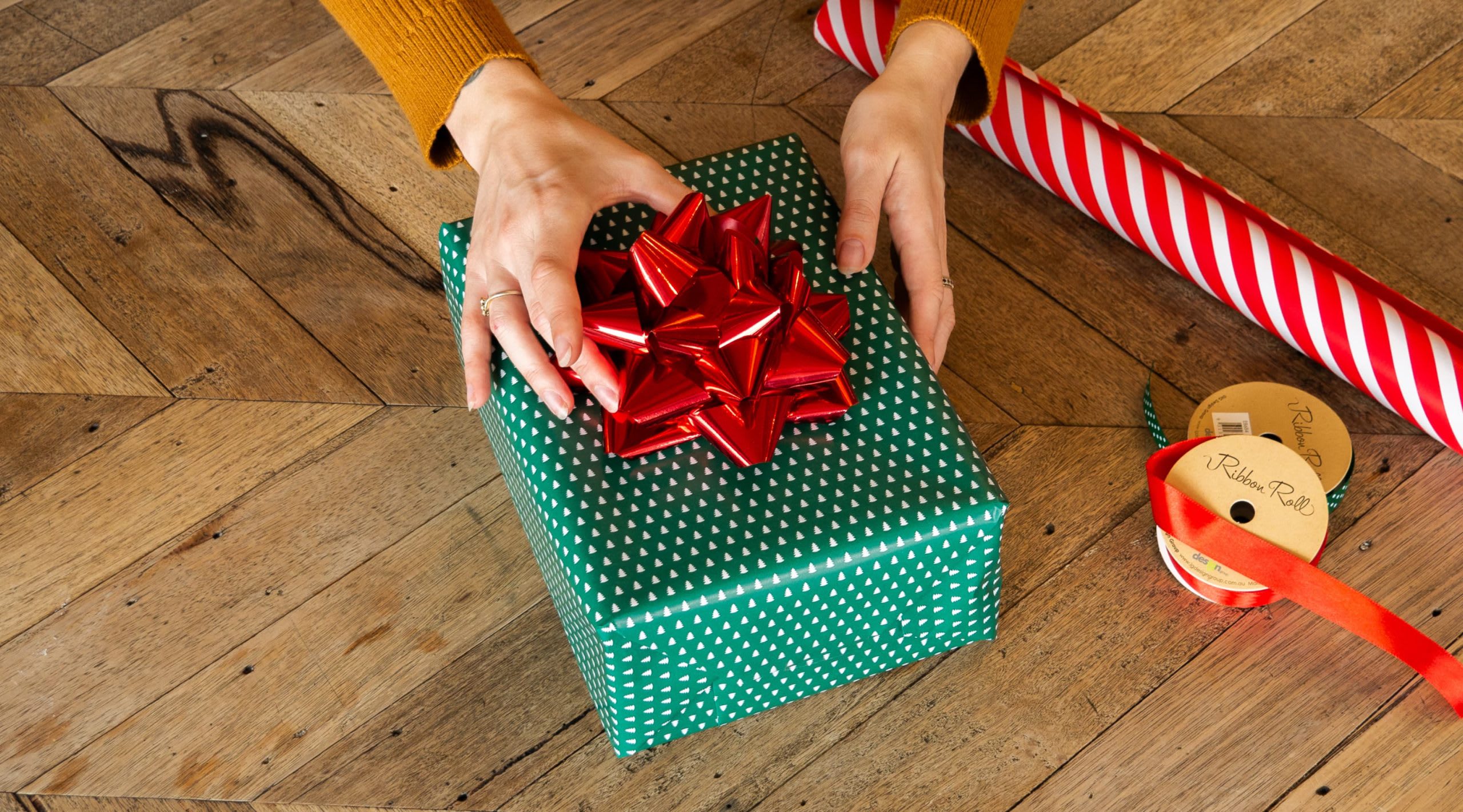 EIne Person platziert eine vorgeformte Schleife auf einem fertig verpackten Geschenk.
