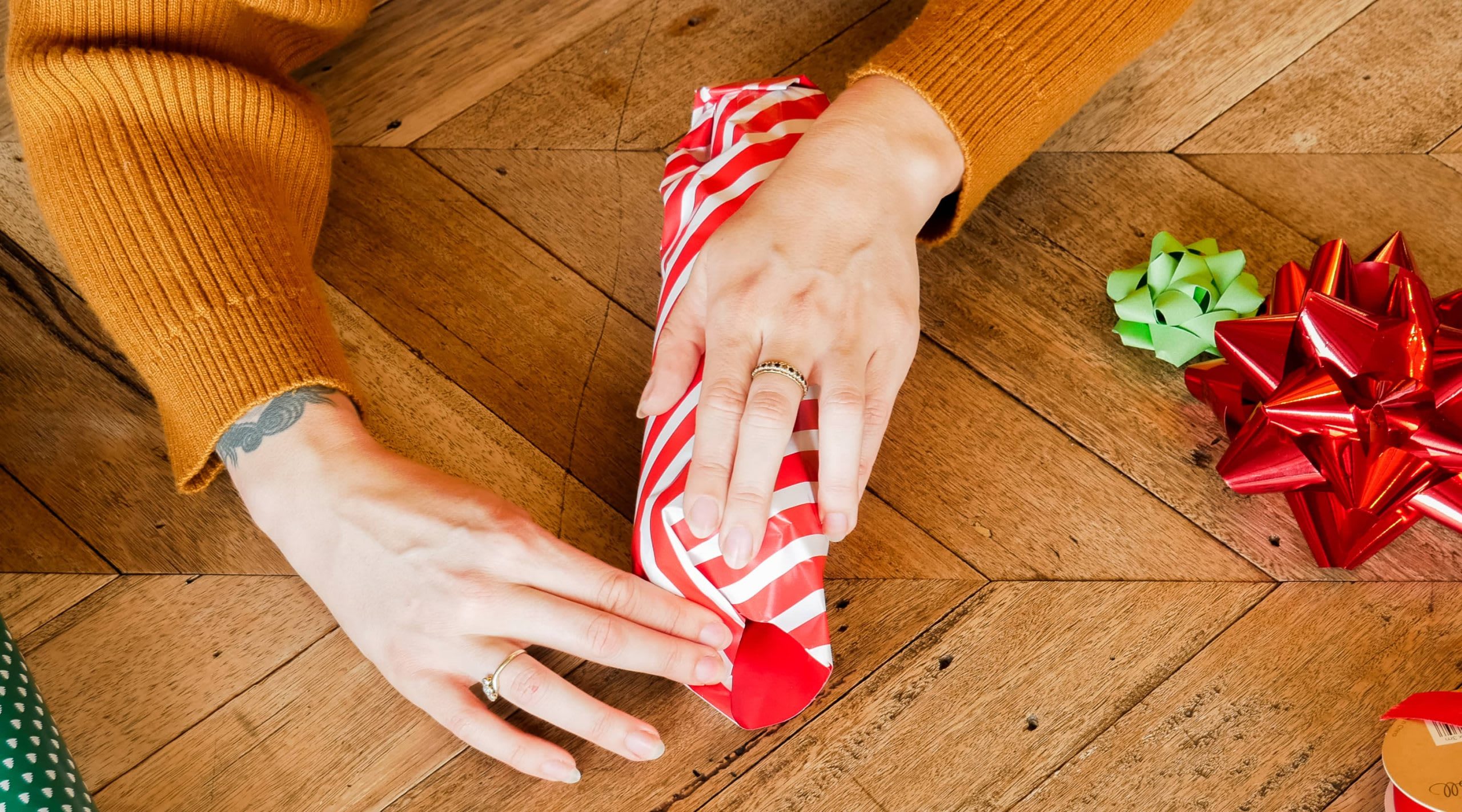 Eine Person legt Geschenkpapier rund um ein zyinderf&ouml;rmiges Geschenk