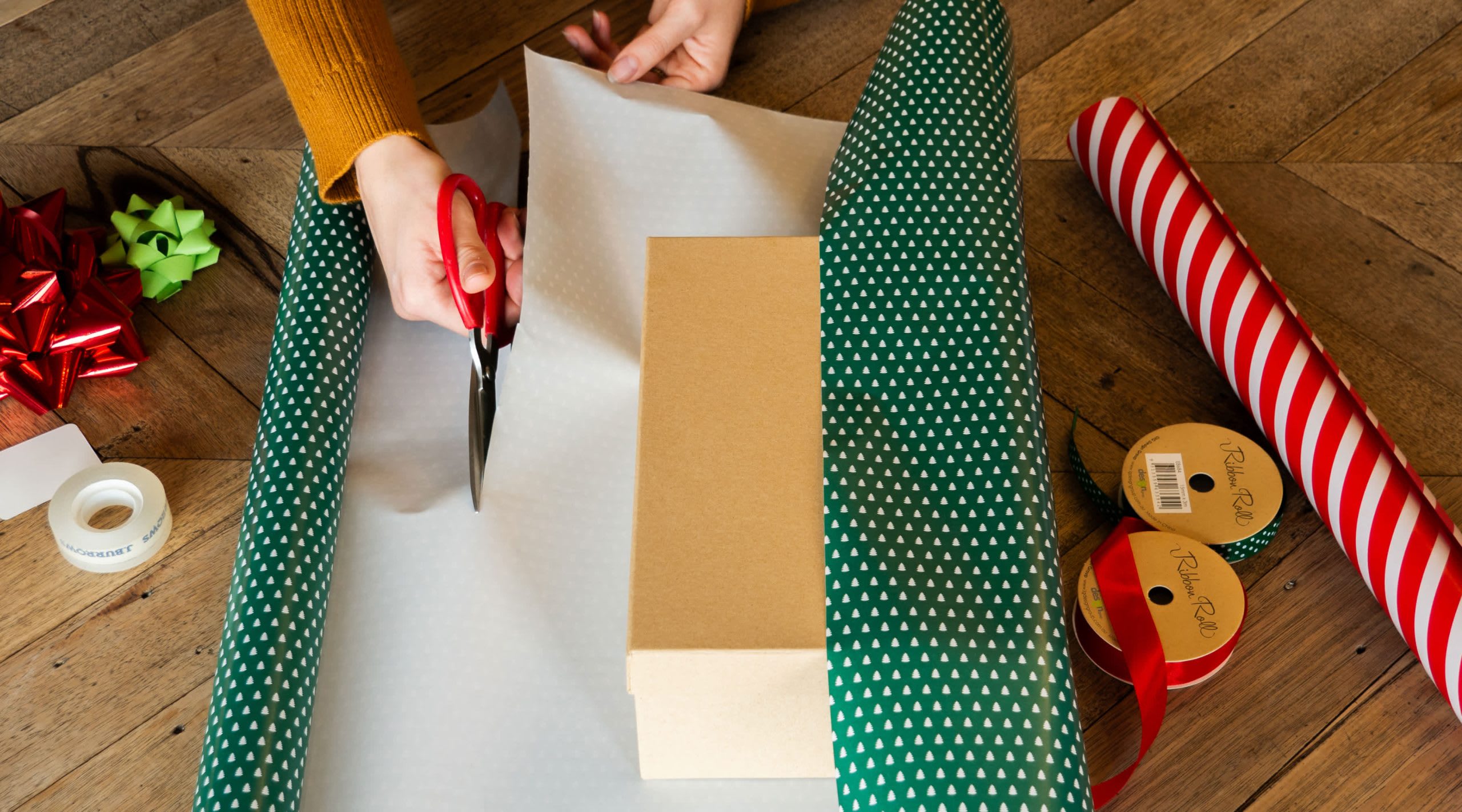 Person schneider Geschenkpapier rund um eine braune Geschenkbox zu 
