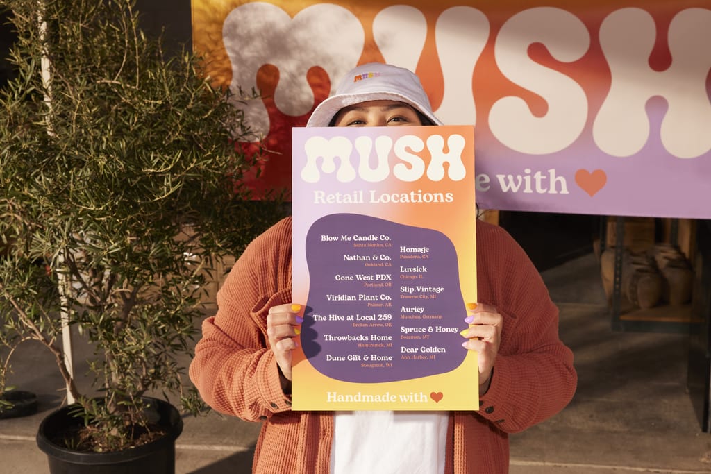 Woman holds retail locations signage, colorful and vibrantly branded hours for Mush.