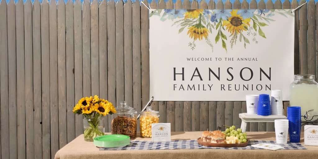 Outdoor event setup with a custom “Hanson Family Reunion” banner featuring sunflower illustrations, displayed above a snack and drink table.
