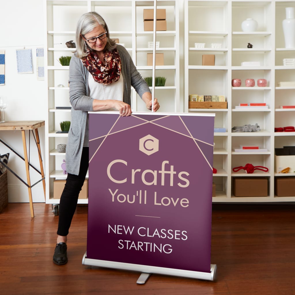 Small business owner pulling up retractable banner in craft shop advertising new classes