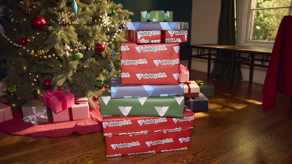 Stack of wrapped gift boxes beside a decorated Christmas tree in a cozy room.