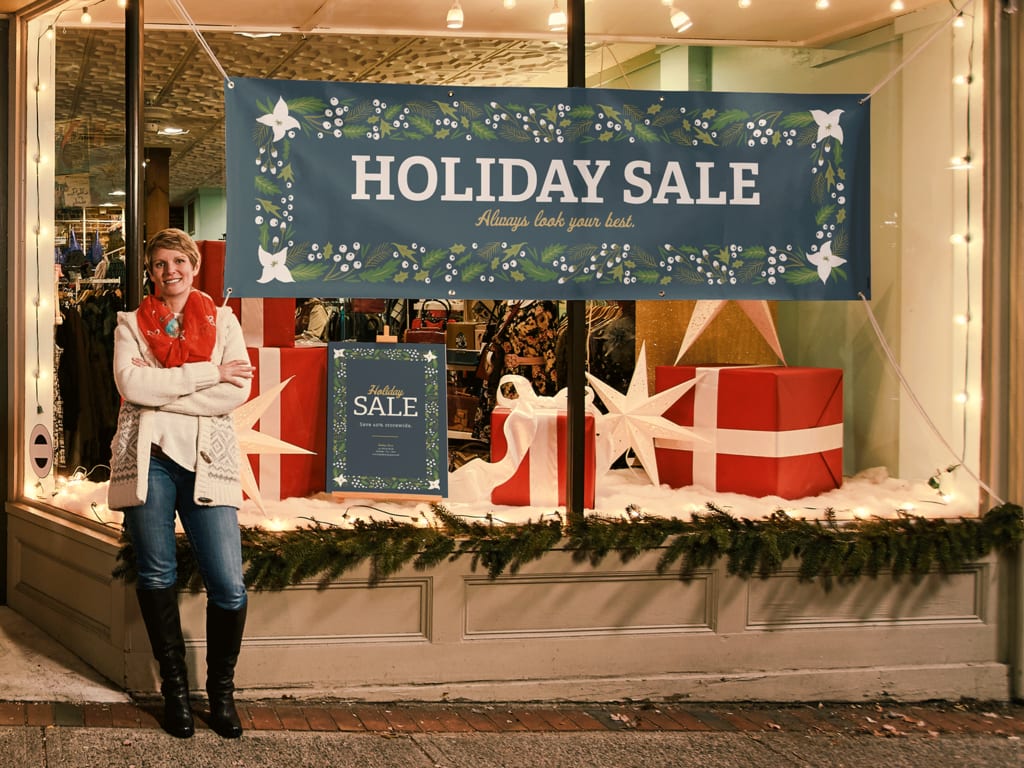 A person standing outside a store with a holiday sale banner