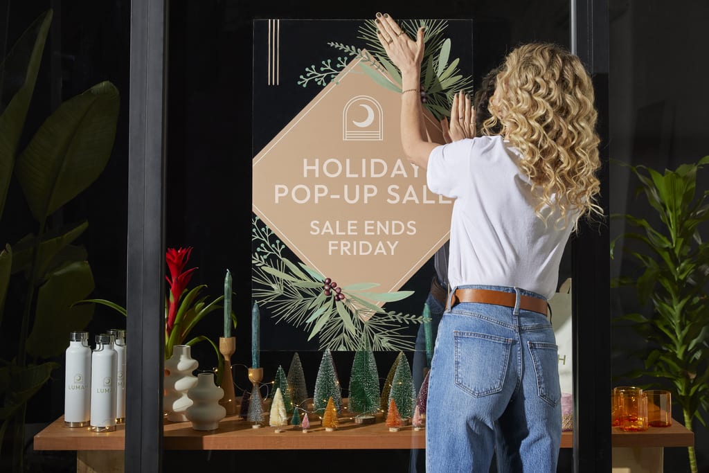 Someone putting up a seasonal storefront sign to promote a holiday sale