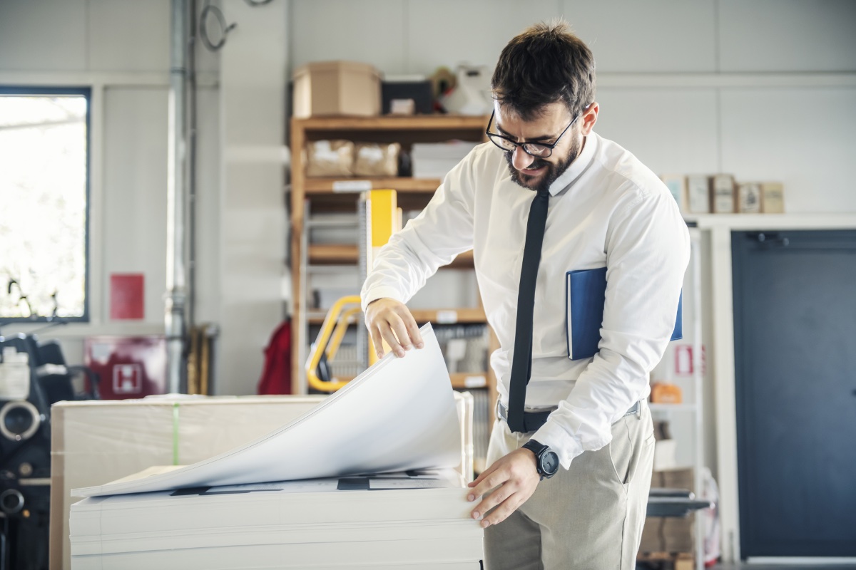 A man in a printing shop holding a large stack of paper