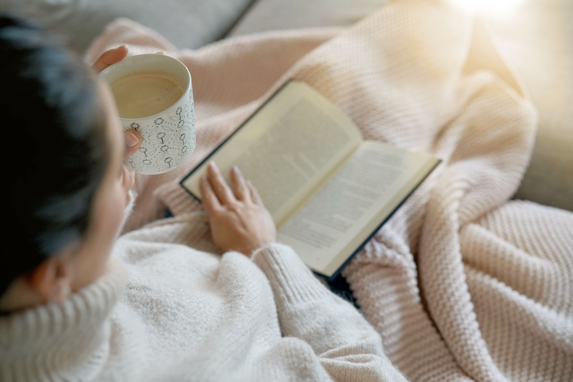 Cosy brunette at home on couch with hot drink and reading