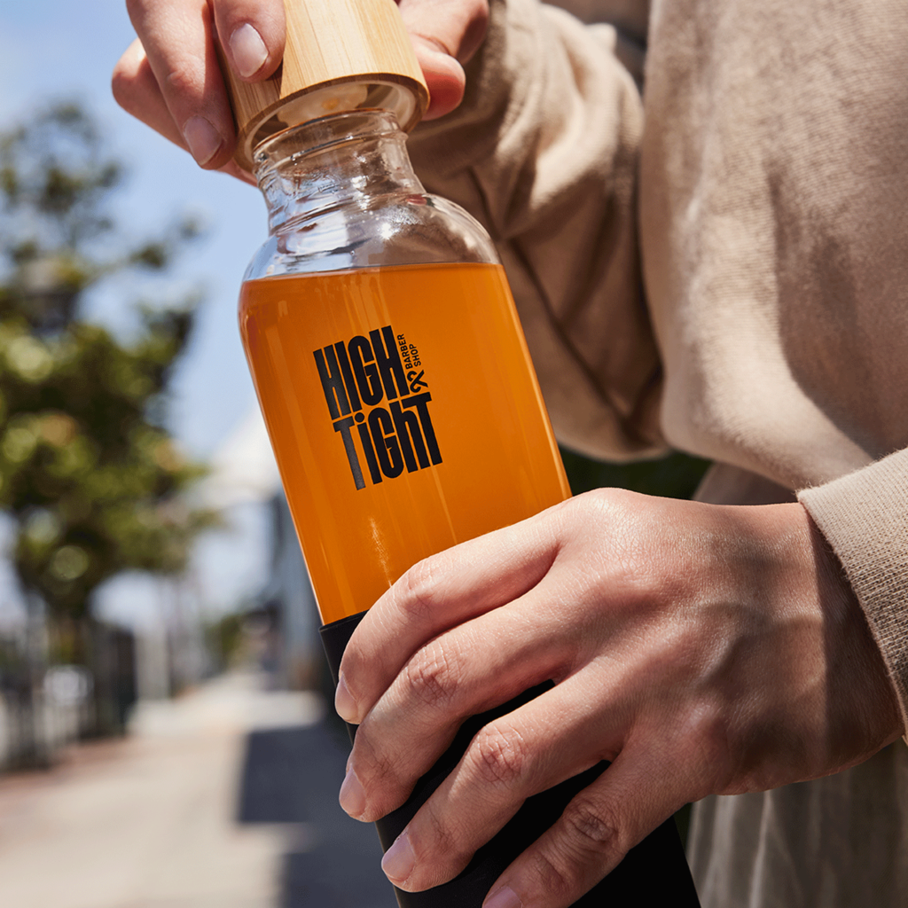 Hands uncapping a bambook lid from a stylish, custom glass water bottle branded with in bold, blocky font-based logo