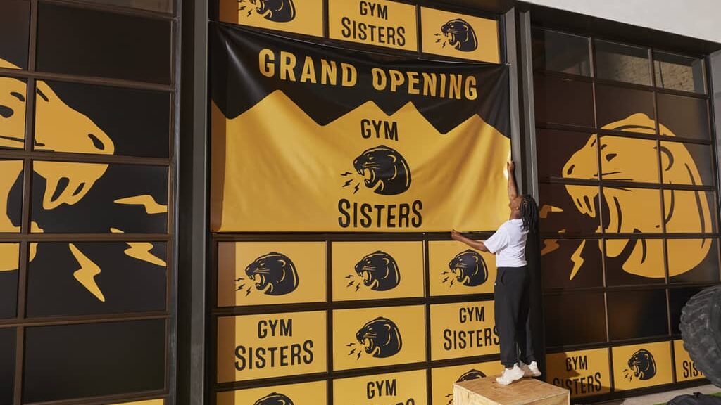 Small business owner hanging a branded yellow banner in a gym for a grand opening