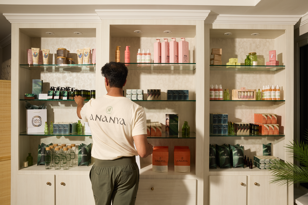 Employee wearing a branded T-shirt arranging products on shelves in a spa retail space