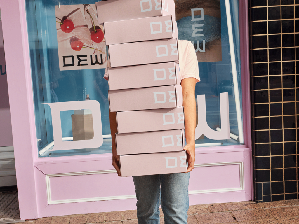 Small business owner holding stack of simple pink custom packaged outside shop, obscuring their face