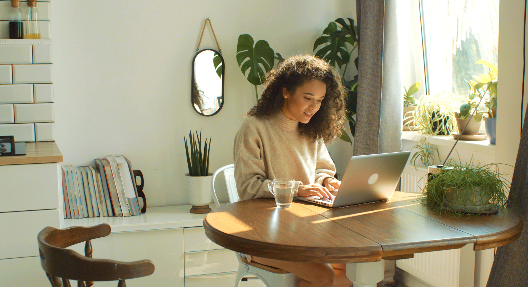woman typing on a laptop next to a window surrounded by plants