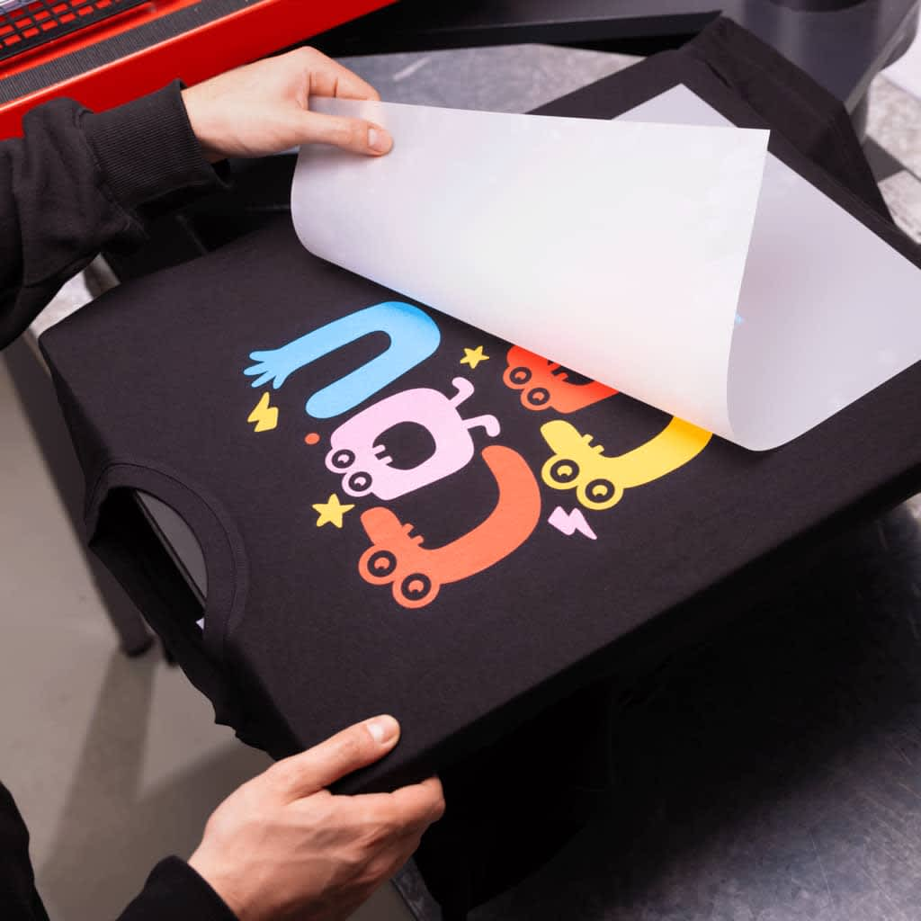 Printing paper pulled back to reveal a colorful design printed on a black T-shirt