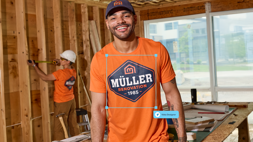 Two construction workers on a building site wearing orange T-shirts with large logo on the font