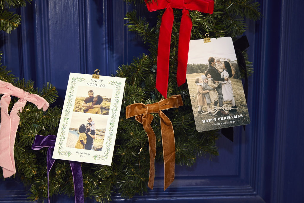 Two family photo Christmas cards hanging from a decorated Christmas tree with colorful velvet bows.