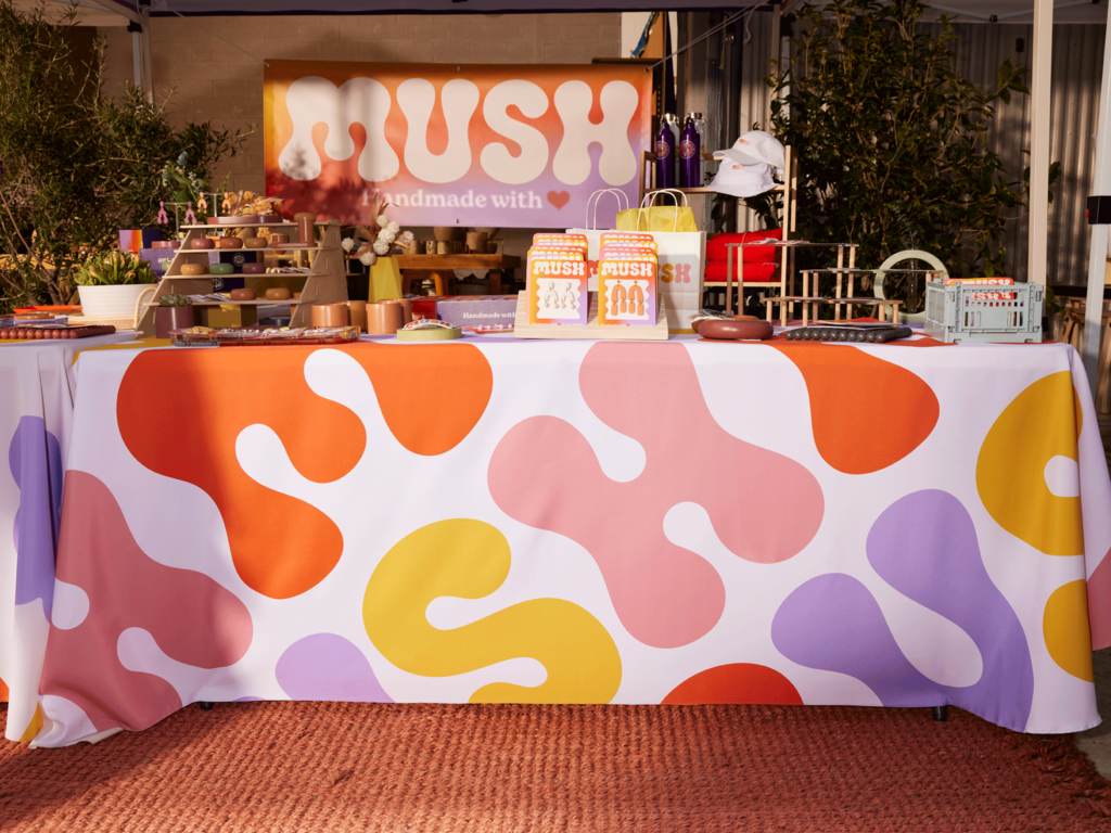 Colorful MUSH market stall with branded tablecloth, signage and handmade products on display.