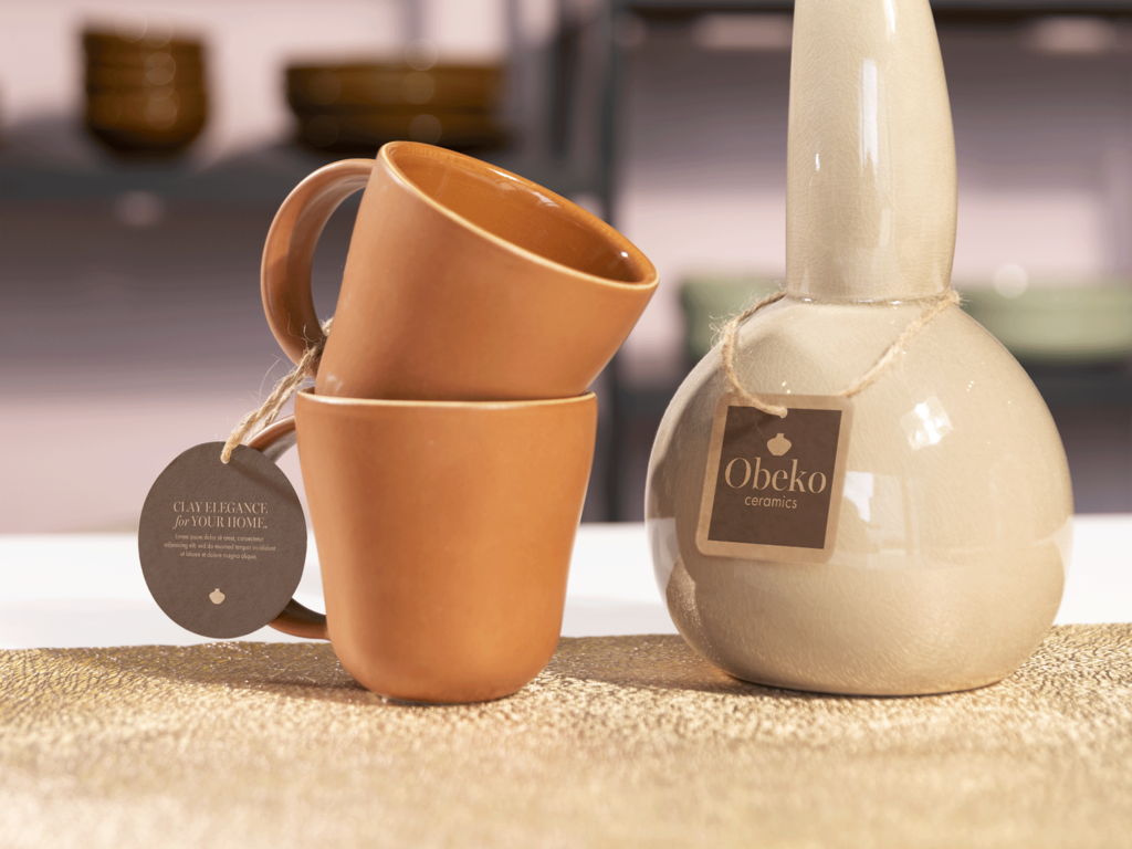 Two orange ceramic mugs and a beige ceramic vase with brown custom tags hung with jute twine